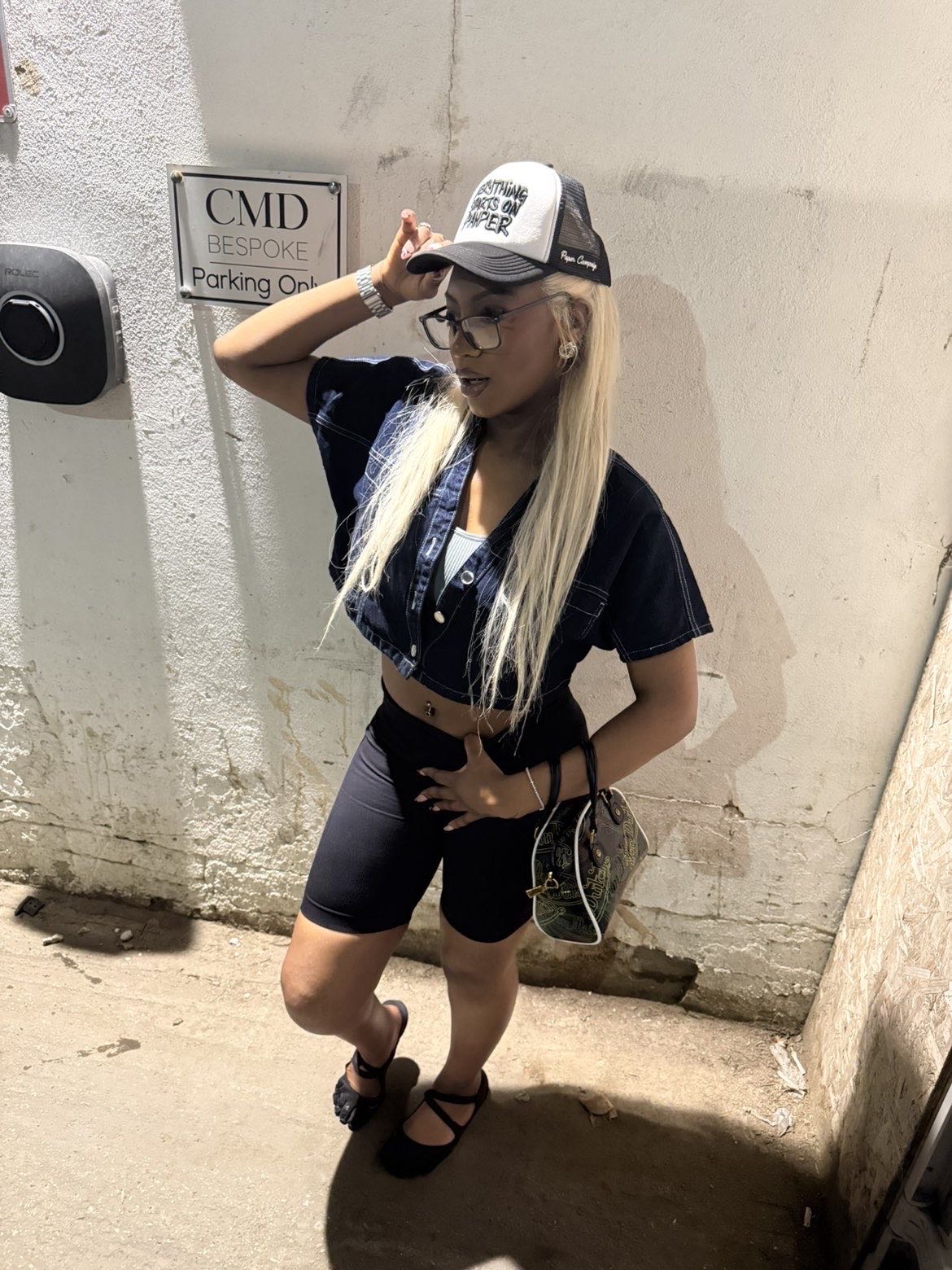 Model against a light wall wearing a black and white Paper Campaign trucker cap and denim crop top